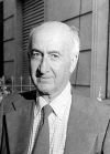 Black and white photo of a bald man looking straight wearing a suit and a tie